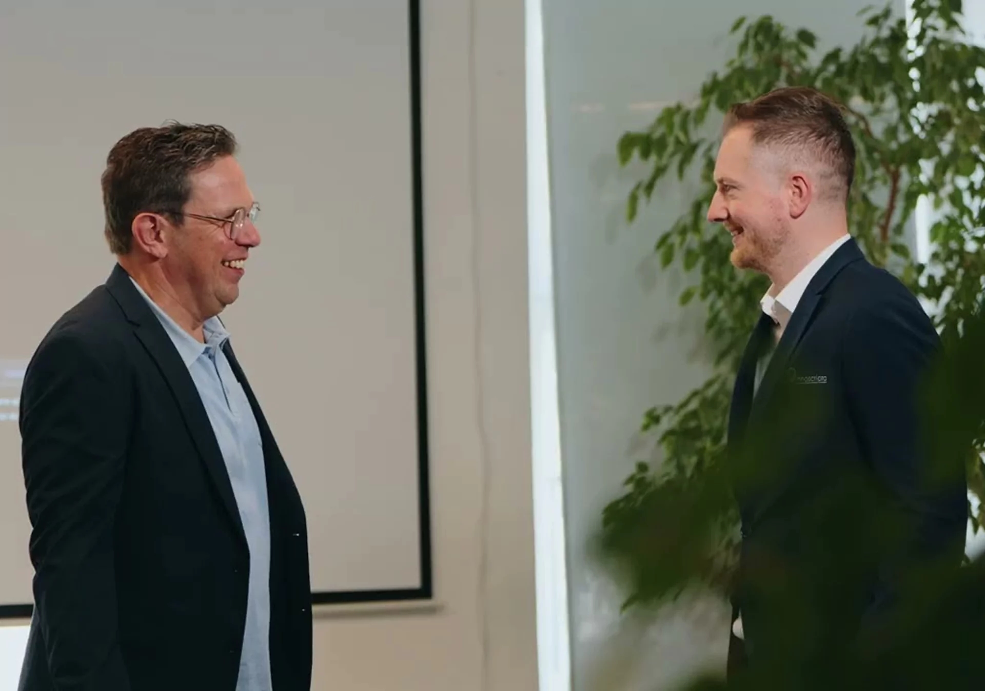 Two business professionals in formal attire having a conversation in a modern office environment, representing collaboration and innovation in R&D management.