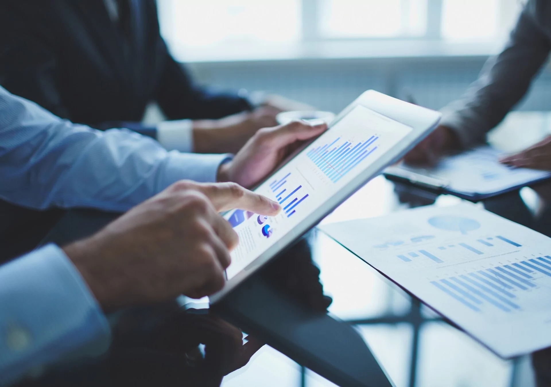 Business professionals analyzing financial charts on a digital tablet and printed documents during a meeting