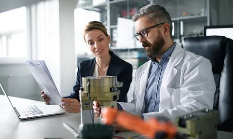 Engineer wearing a lab coat and helmet analyzing a digital interface with technical schematics in a high-tech industrial facility