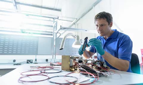 Engineer working on dual monitors displaying 3D CAD models of mechanical parts in a design software interface